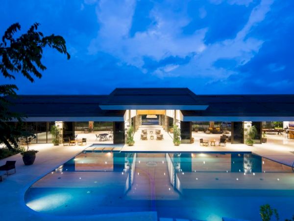 A modern building with a large, illuminated swimming pool at night, surrounded by lounge chairs and open spaces.