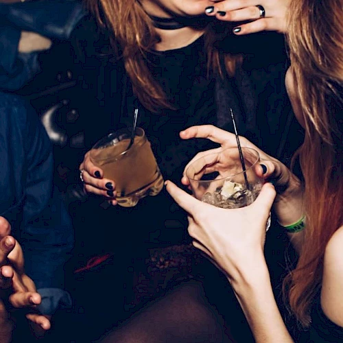 People are gathered, holding drinks with ice, chatting and laughing, possibly at a social event or party, creating a lively atmosphere.