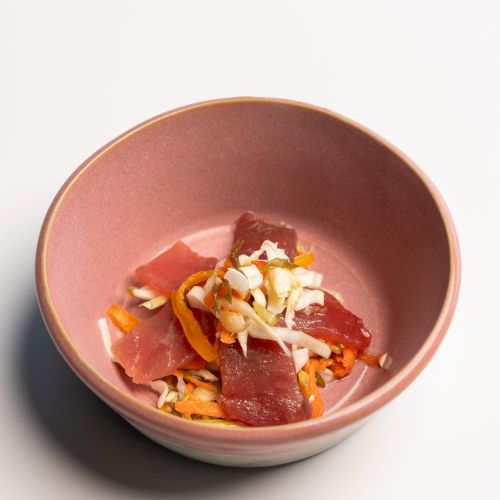 A bowl with sliced raw fish, possibly tuna, atop shredded vegetables and garnished with a bit of chopped slaw.
