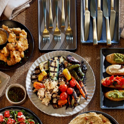 A vibrant spread of grilled veggies, falafel, salad, flatbreads, and dips arranged on plates with forks and napkins for a festive meal.