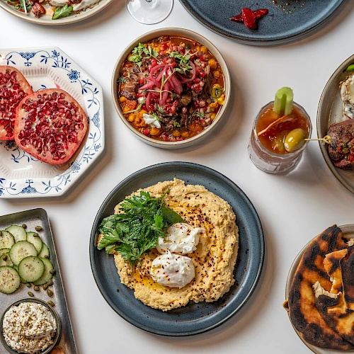 A spread of dishes: steaks, bowls, fried eggs, grilled meat, mashed potatoes with herbs, grilled flatbread, and sides on blue/white ceramics.