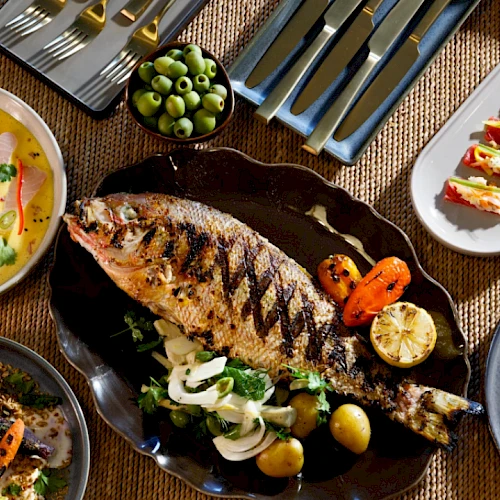 A lavish spread: grilled fish centerpiece with herbs, creamy sauces, quiches, olives, vibrant veggies, small bites, and assorted sides for sharing.