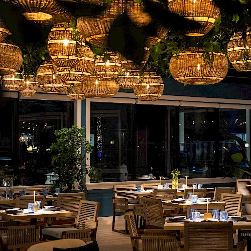 A stylish restaurant with warm hanging lanterns, wicker chairs, and neatly set tables for dinner, creating a cozy, chic dining atmosphere.