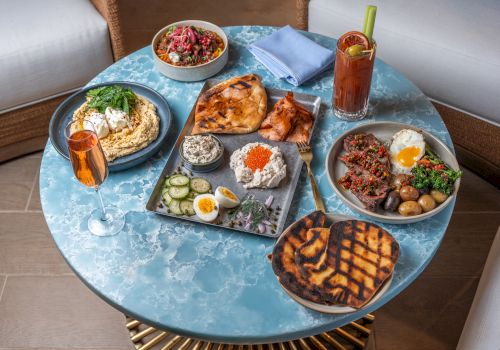 Middle Eastern feast: hummus, pita, kebabs, salads, eggs, potatoes, and a juice drink served on a table.