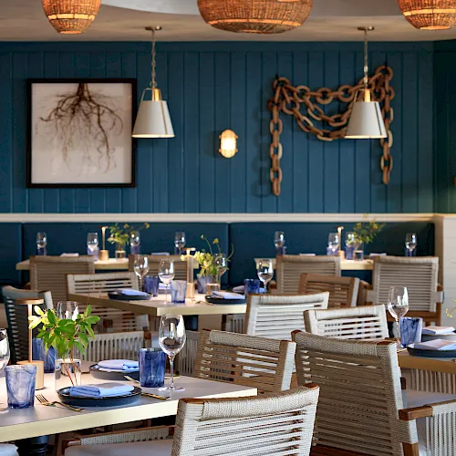 A stylish restaurant dining area with set tables, blue walls, hanging wicker lanterns, and warm pendant lights above.