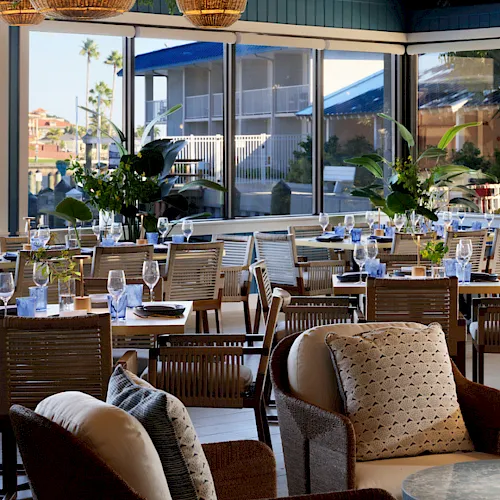 A stylish patio restaurant with hanging wicker lanterns, set tables and chairs, and large windows overlooking the courtyard.