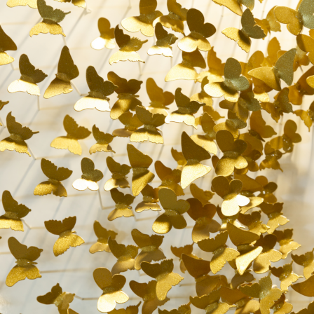 Golden butterfly confetti scattered across white tiled floor, sparkling in sunlight.